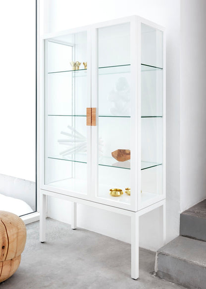 Designed by Anya Sebton and Eva Lilja Löwenhielm 2014.  Glass cabinet with lacquered MDF frame, stand in lacquered metal, doors and sides in glass with twined leather handles. Including two glass shelves.