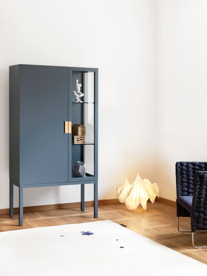 Designed by Anya Sebton and Eva Lilja Löwenhielm 2014.  Glass cabinet in lacquered MDF, stand in lacquered metal. The left side has a covered door and a covered side with two lacquered shelves and the right side has a glass door and a glass side with two glass shelves. Doors have twined leather handles. 