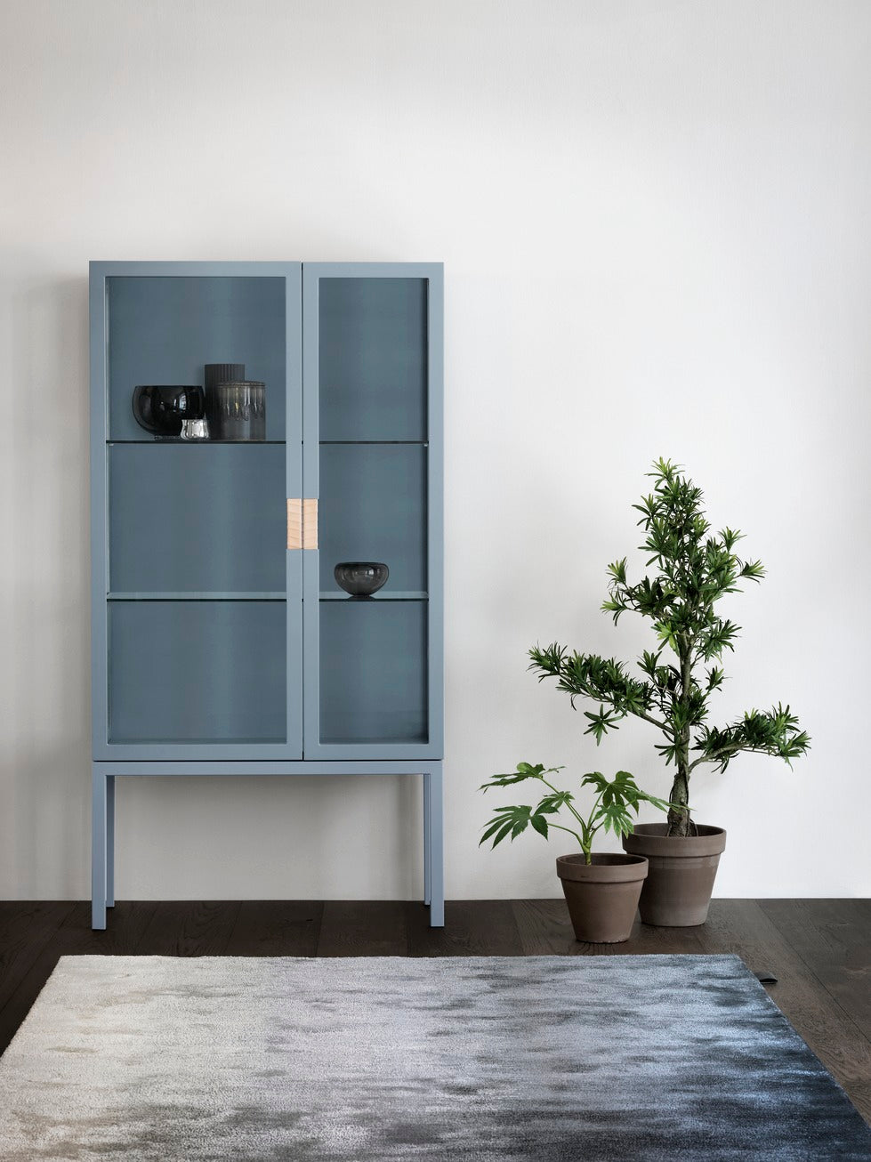 Designed by Anya Sebton and Eva Lilja Löwenhielm 2014.  Glass cabinet with lacquered MDF frame, stand in lacquered metal, doors and sides in glass with twined leather handles. Including two glass shelves.